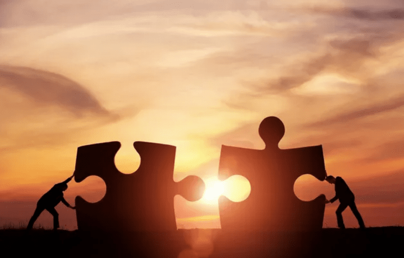 Two puzzle pieces silhouetted against a warm sunset sky, symbolizing connection.