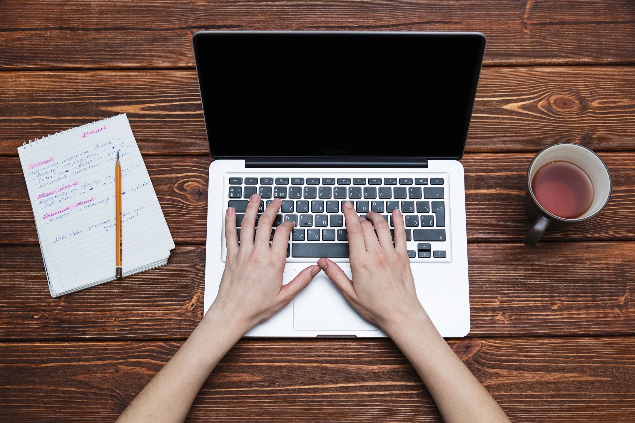 Hands typing on a laptop keyboard on a wooden table.